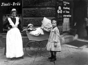 Nanny with children, ca. 1910, A woman with two children in front of a historical building with