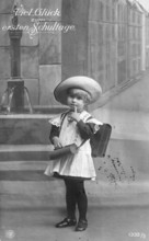 School enrolment, 1920s, A child poses with a school bag and hat in front of a painted city motif,