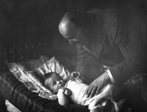 Man and baby, 20s, 1920s, A man bends lovingly over a baby lying in bed, Historical photo