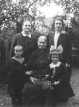 Family photo, 1920s, Three generations pose for a portrait in the garden with flower decoration,
