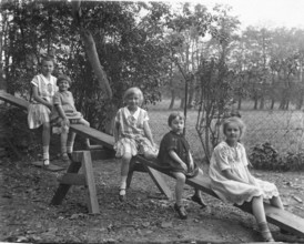 Five children on a seesaw, 1920s, Five children sitting on a swing outdoors, black and white