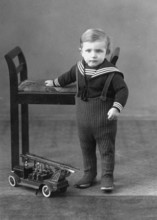 Little boy, toy, fire engine, 1920s, A toddler in a sailor suit stands next to a chair and a toy