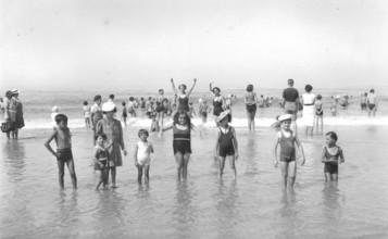 Children in the water, 1920s, Children playing in shallow water on the beach under a clear sky. A