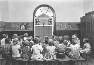 Puppet theatre, 1920s, children sit in a classroom and watch a puppet show. The walls are