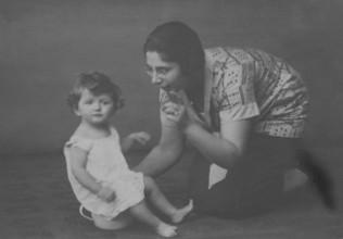 Mother with peeing childBeach, Baltic Sea, 1930s, A mother kneels next to her sitting child, both