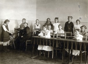 Sewing class at school, 1920, girls in a classroom practising sewing while a teacher sits at a