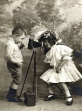 Children's camera self-timer 1906, Two children playing with an old camera, one looking at the