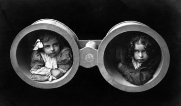 Two girls in binoculars, 1920s, Two children looking through oversized binoculars in a black and