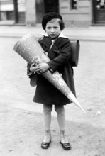 Little girl with school cone, 1940, A child in school uniform holding a large sugar cone on the
