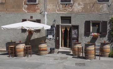 Enoteca with wooden barrels as tables and bar stools under a large parasol in front of an old house