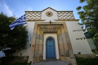 White facade of a building with Greek flag and blue door, Kos Town, Synagogue, Kos, Dodecanese,