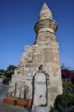 Historic fountain next to a stone tower under a clear blue sky, Eski Cami, Minaret, Kos Town, Kos,