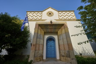 Greek architecture with turquoise door and flag on bright, sunny background, Synagogue, Kos Town,
