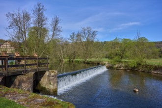 A weir in the river leads to a small waterfall, surrounded by trees, spring, Obersinn, Sinntal,