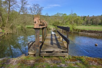 Wooden footbridge over a body of water in a natural setting with trees in the background, spring,