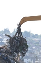 Hydraulic crane lifts scrap metal at the scrapyard in the background a city