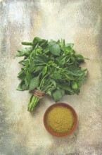 Ground green basil, in a ceramic bowl, with a bouquet of fresh green basil, on the table, top view,