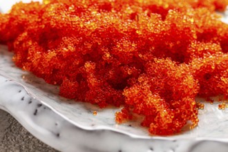 Orange Tobiko flying fish caviar, on a light blue plate, caviar for rolls and sushi, close-up