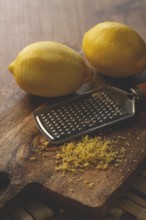 Lemons and grated orange peel, with a zest grater, on a chopping board, close-up, no people