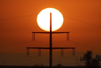 The sun rises behind an electricity pylon near Frankfurt am Main, Frankfurt am Main, Hesse, Germany