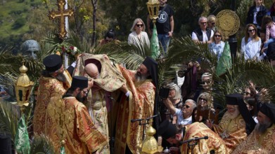 Priests standing under a cross during an outdoor religious ceremony surrounded by worshippers and