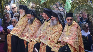 Several priests in golden robes sitting next to each other at an outdoor ceremony, surrounded by