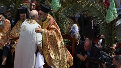 A priest embraces another clergyman during a religious ceremony amidst palm trees, Orthodox