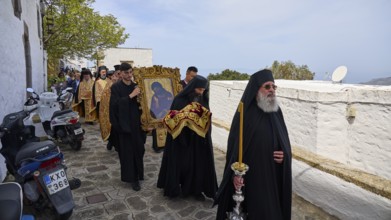 Priests in black robes and icon bearers walk along a wall during a religious procession, Orthodox