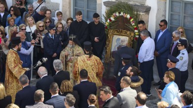 Priests and people gather in a ceremony around an icon, some wearing traditional vestments, others