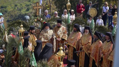 Clergy in richly decorated robes at an open-air ceremony, surrounded by palm trees and spectators,
