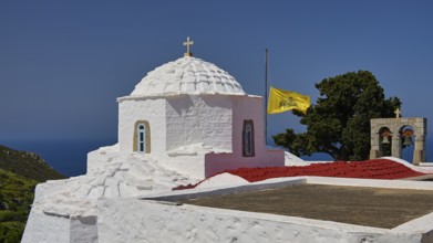 White chapel with dome and waving yellow banner, sea and trees in the background, church, Chora,