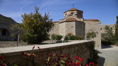 Stone church with tiled roof, surrounded by a blooming garden under a blue sky, woman's monastery,