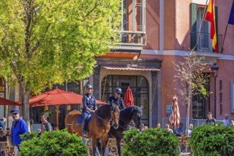 Horses with mounted police in a city square with people and houses with restaurants, Palma de