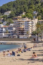 People sunbathing on a sandy beach at a tourist resort with houses close to the shore at the