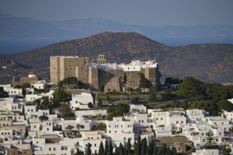 View of a castle above white houses, framed by mountains and the sea, Monastery of St John the