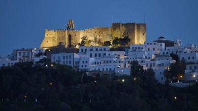 Illuminated castle high above white houses at night, Monastery of St John the Theologian, Monastery