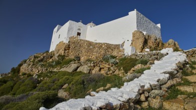 White building with stone steps and vegetation on rocky terrain under a blue sky, Church of the