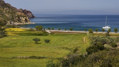 Green landscape with a view of the sea and a sailing boat, surrounded by mountains, Lambi Beach,