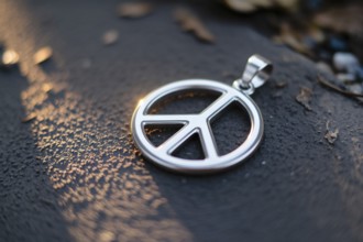 Silver peace symbol pendant lying on rough ground as metaphor for peace in times of war. Generative