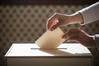 Woman's hands casting vote by placing folded ballot paper into voting box during election.