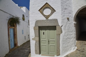 Green door with geometric frame in a white historic building with plants, Mantomata stones, Chora,