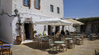 Cosy café terrace with parasols and rustic white buildings in the background, Platia Lesvias,