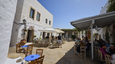 Outdoor café with tables and chairs on a sunny terrace next to white houses, Platia Lesvias,