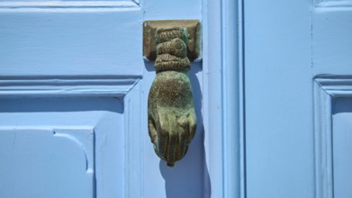 A metallic, hand-shaped door knocker on a blue door, depicted in detail, Chora, UNESCO World