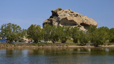 Rock rises behind a row of trees on the lakeshore under a clear sky, Rock of Kalikatsou, Seasonal