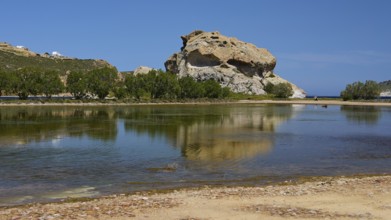 Large rock reflected in a calm lake under a blue sky, Rock of Kalikatsou, Seasonal Salt Lake,