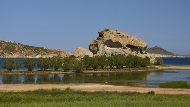 Massive rock formation surrounded by water and trees under a clear sky, seasonal salt lake, Grikos,