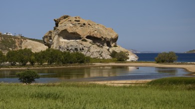 Dominant rock structure over an open water surface with green shore vegetation, Rock of Kalikatsou,