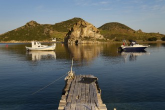Two boats lying on calm water in front of rocky coastal landscape with wooden jetty in the