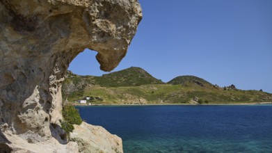 Large rock overlooking the clear blue sea with green hills in the background, Tragonisi Island,